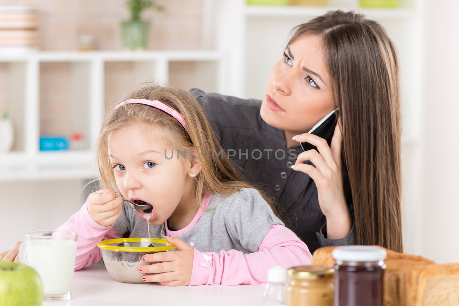 Overworked Business Woman and her little daughter in the morning. Overworked mother make phone calls before going to work. Daughter eating cereal with milk.