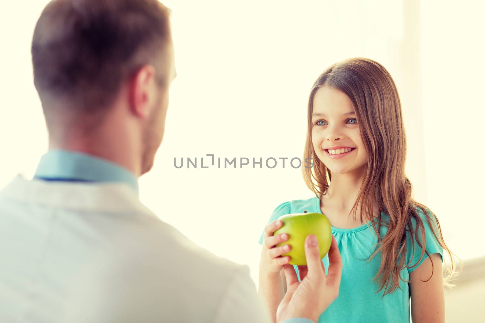 male doctor giving an apple to smiling little girl by dolgachov