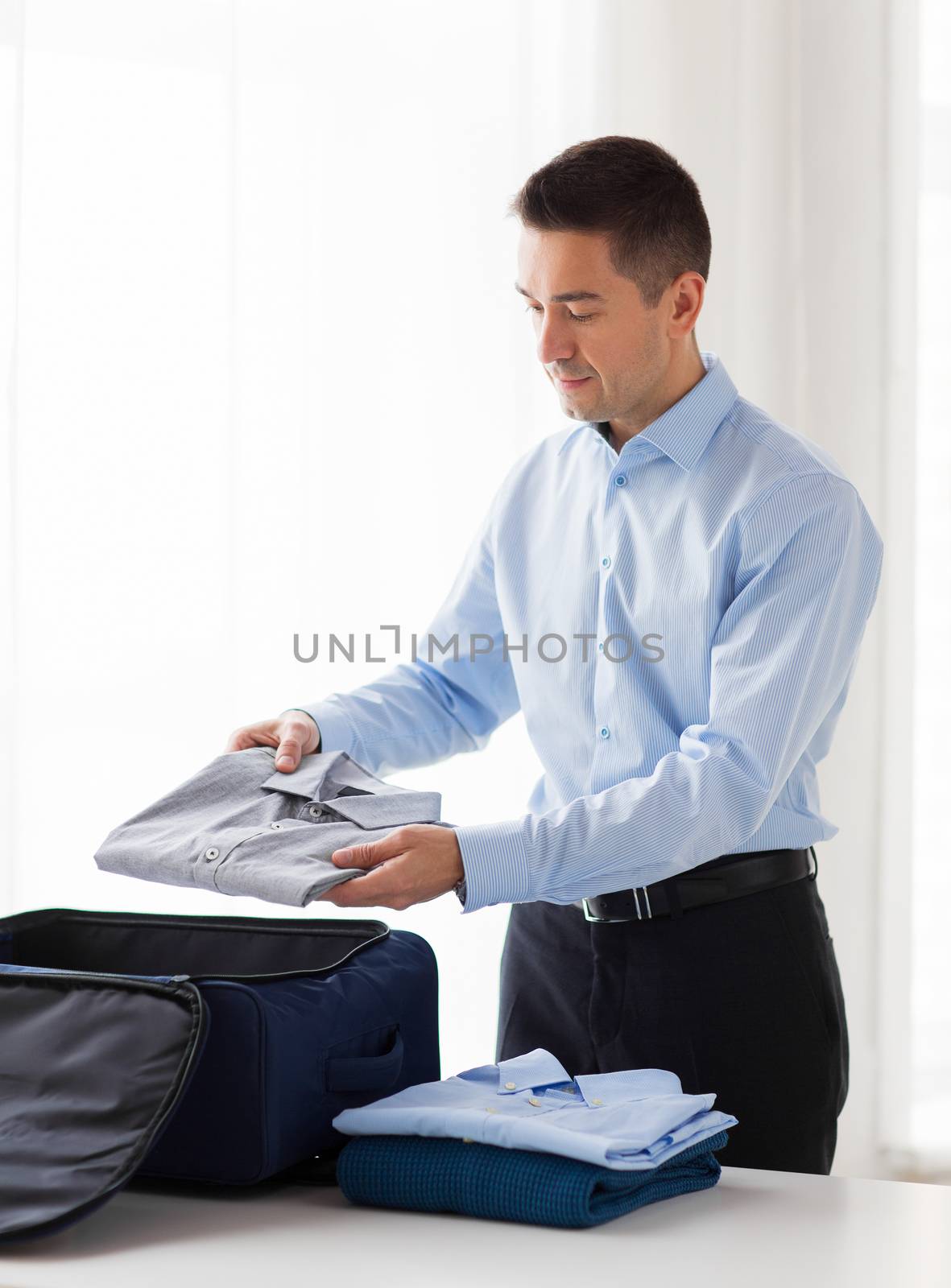 business, trip, luggage and people concept - happy businessman packing clothes into travel bag
