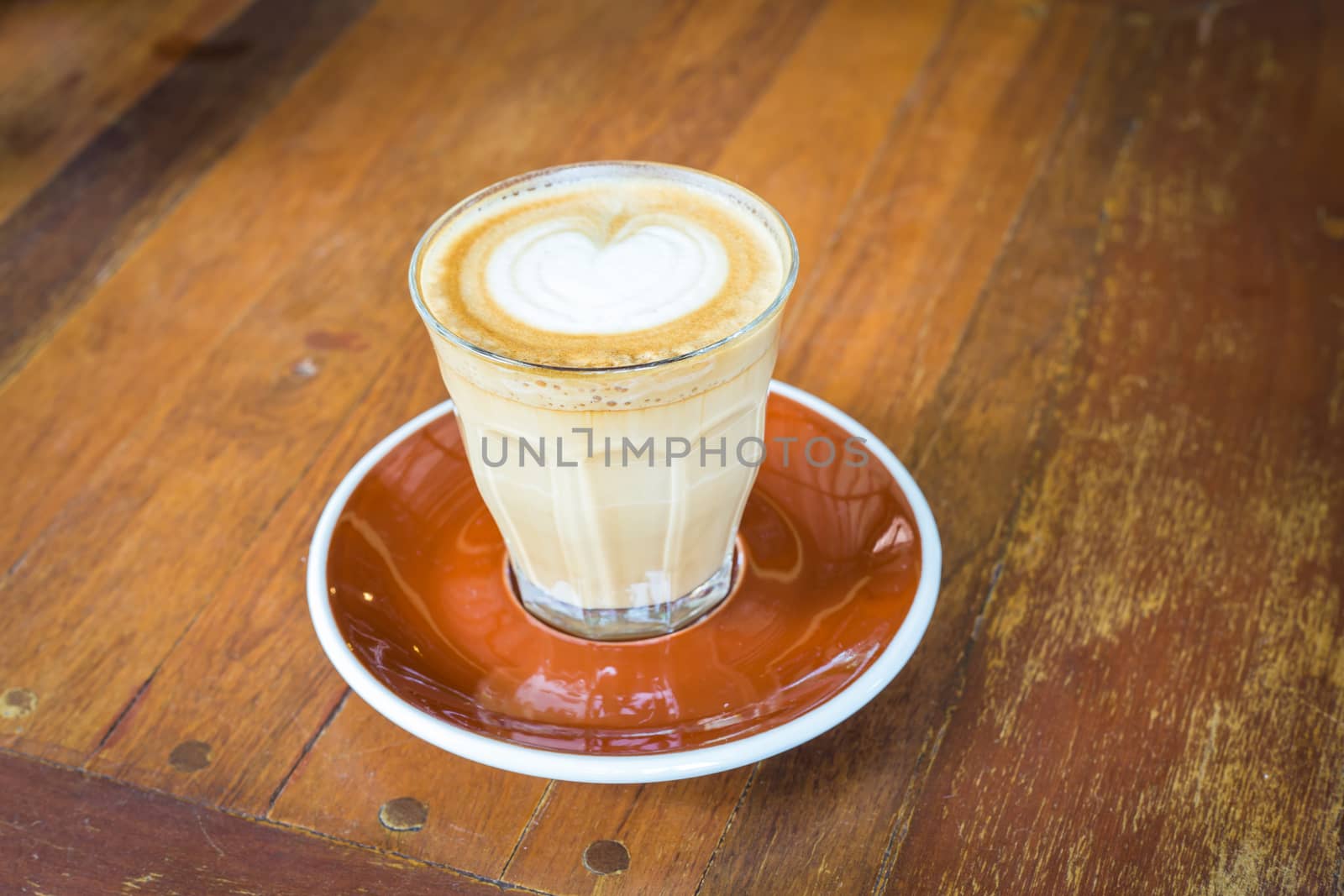 latte art coffee in glass clear cup on wood table by powerbeephoto