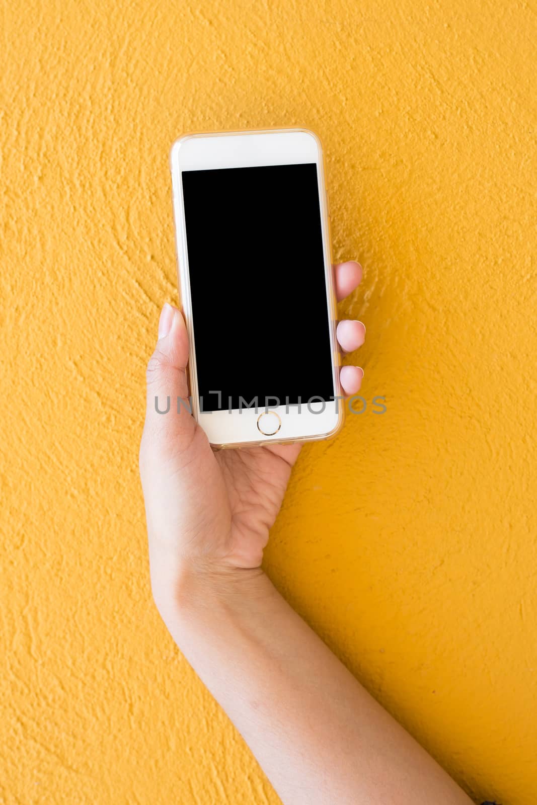 Hand holding white Smartphone on yellow wall background