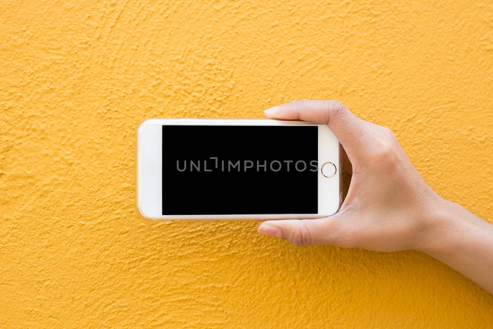 Hand holding white Smartphone on yellow wall background by powerbeephoto