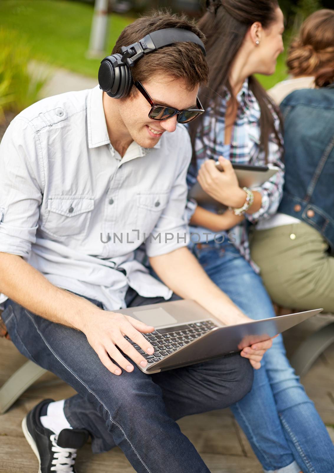 summer, education, technology and people concept - group of students or teenagers with laptop computers sitting on bench outdoors