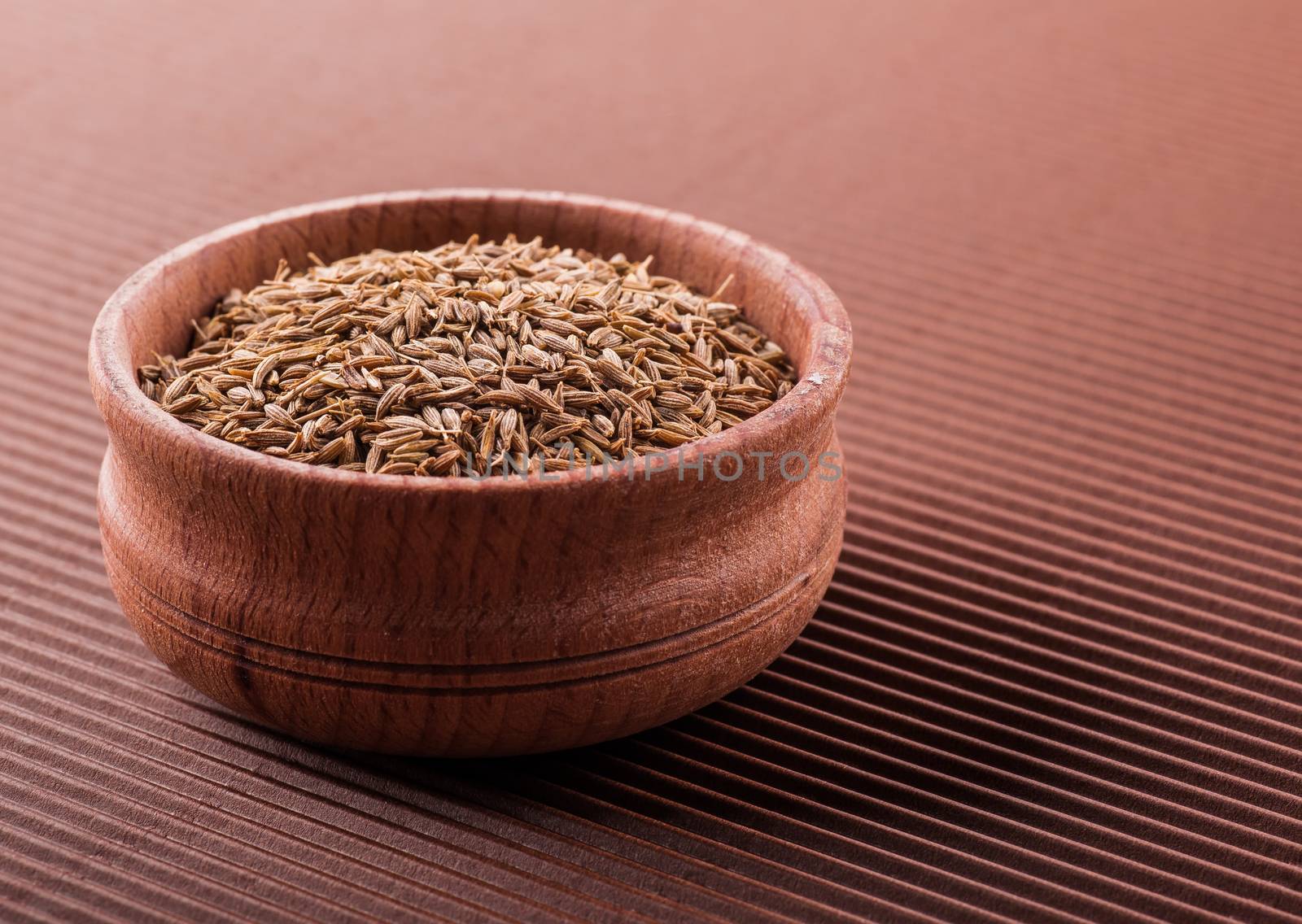 cumin in a wooden bowl on a brown background