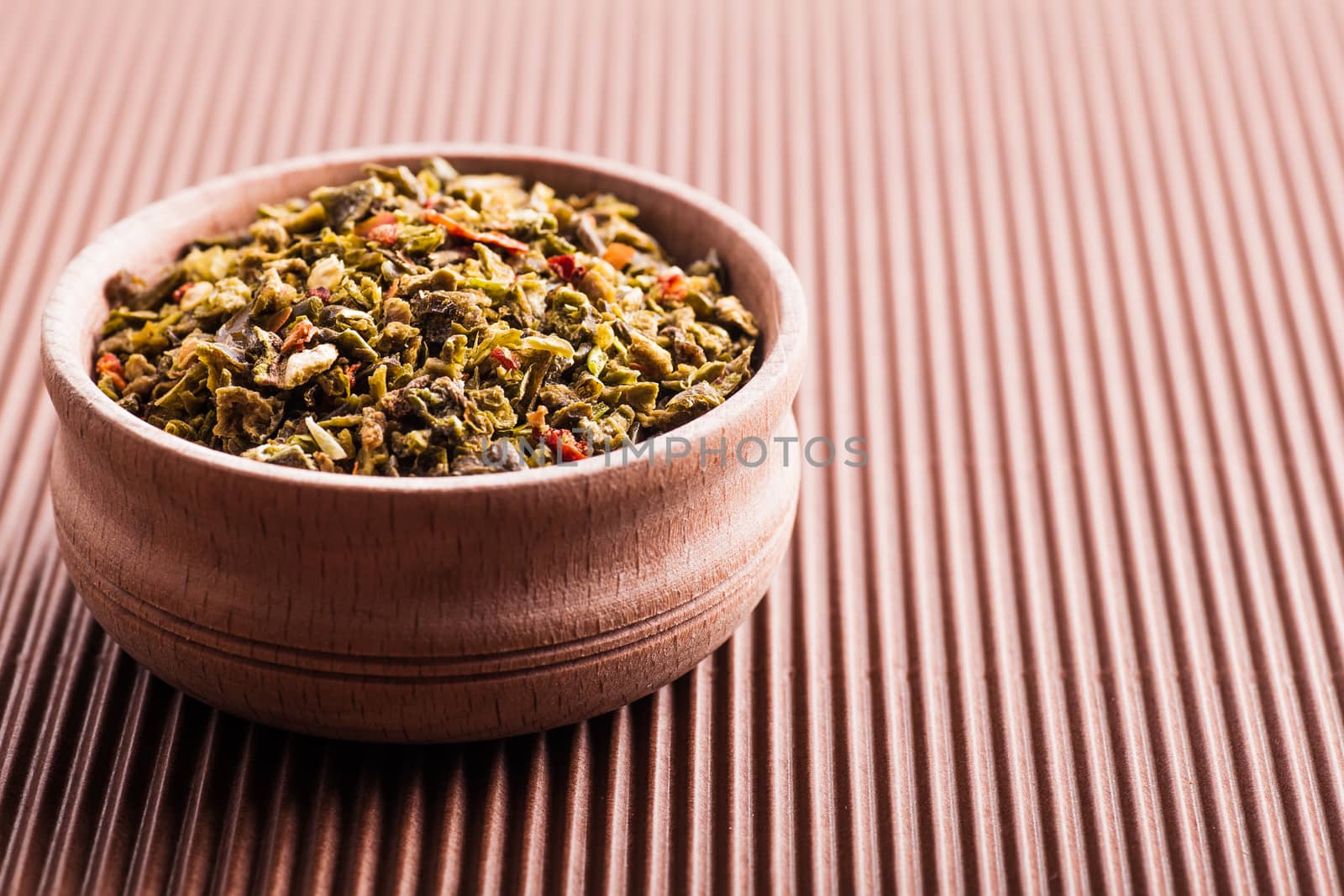 dry spice green pepper in a wooden bowl on a brown background