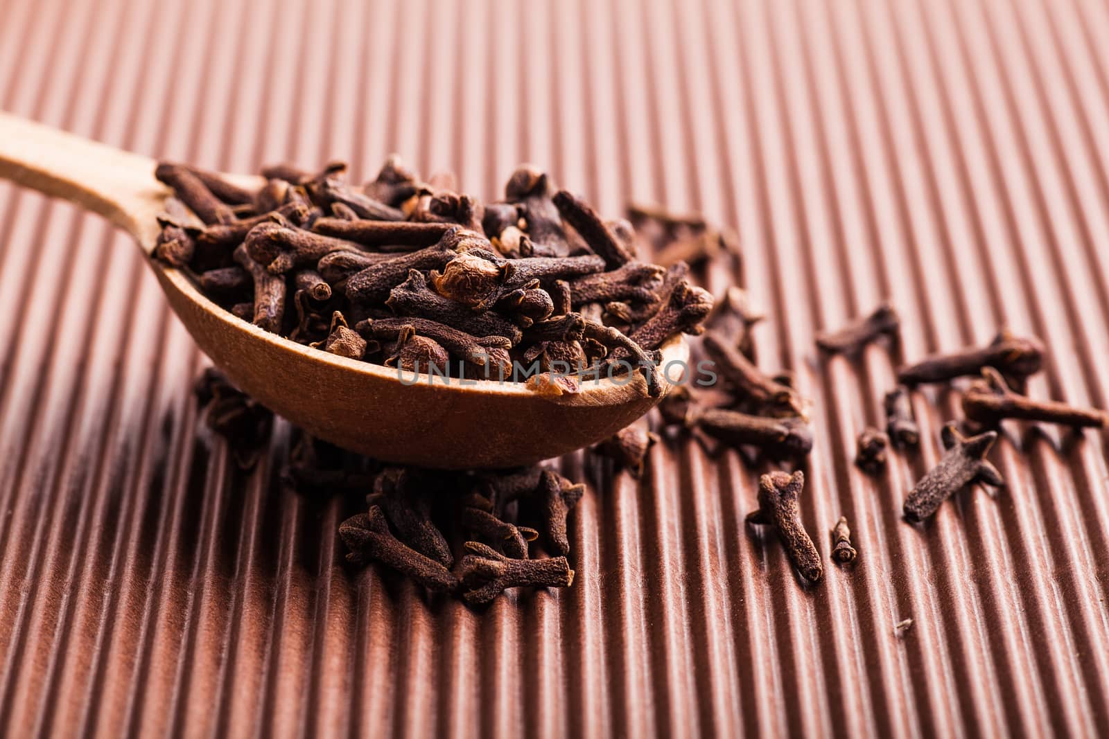 clove in a wooden spoon on a brown background