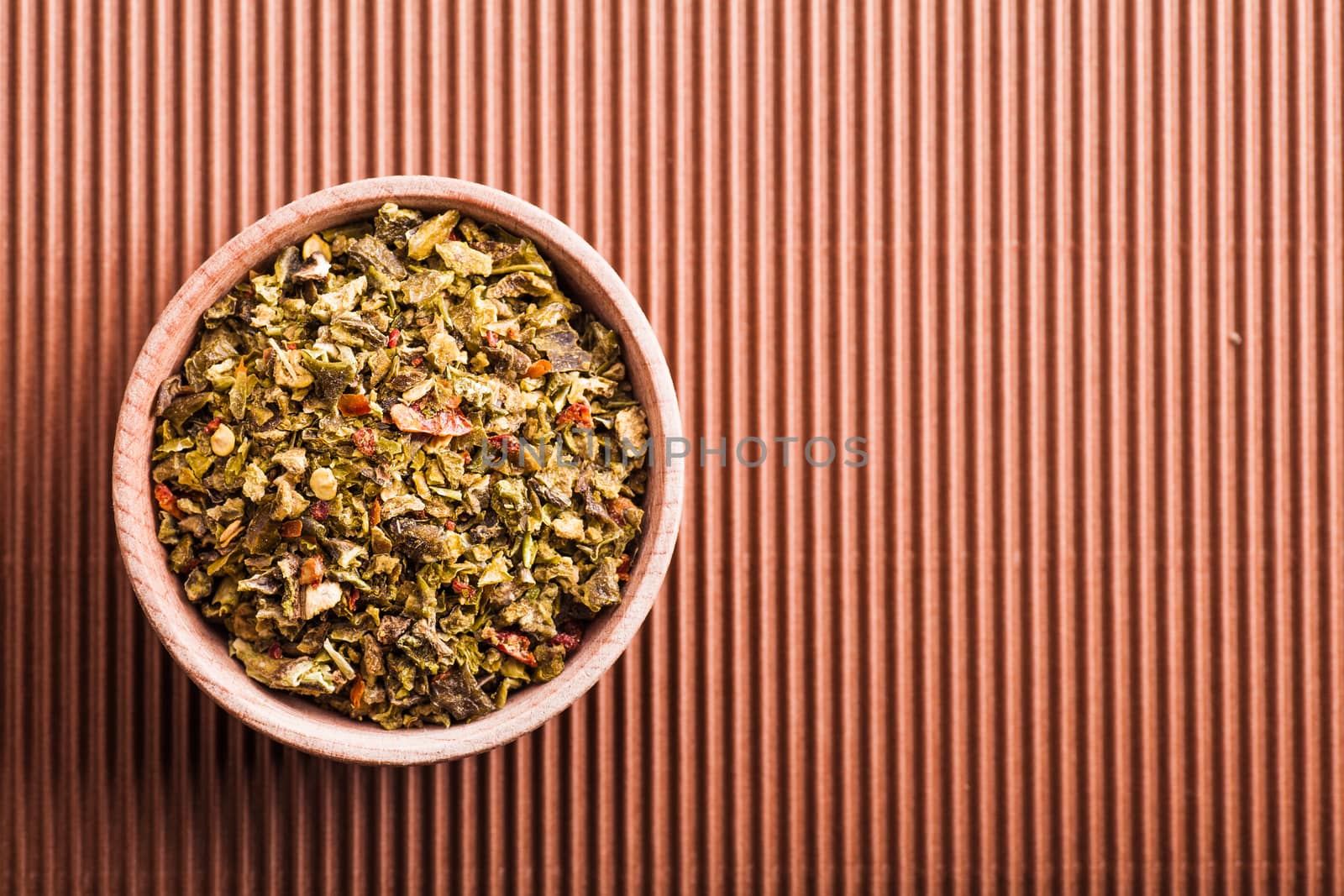 spice green pepper in a wooden bowl on a brown background