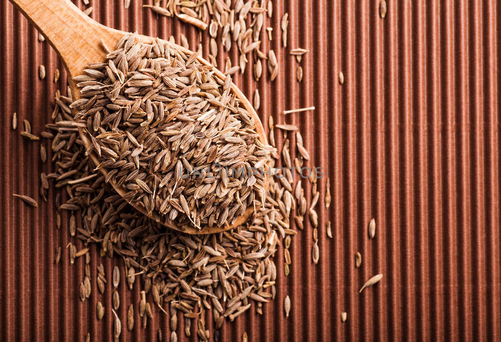 cumin in a wooden spoon on a brown background