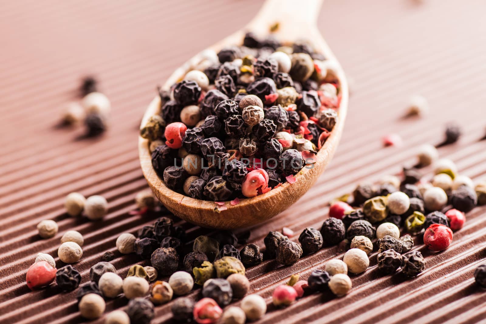 assorted pepper in a wooden spoon on a brown background