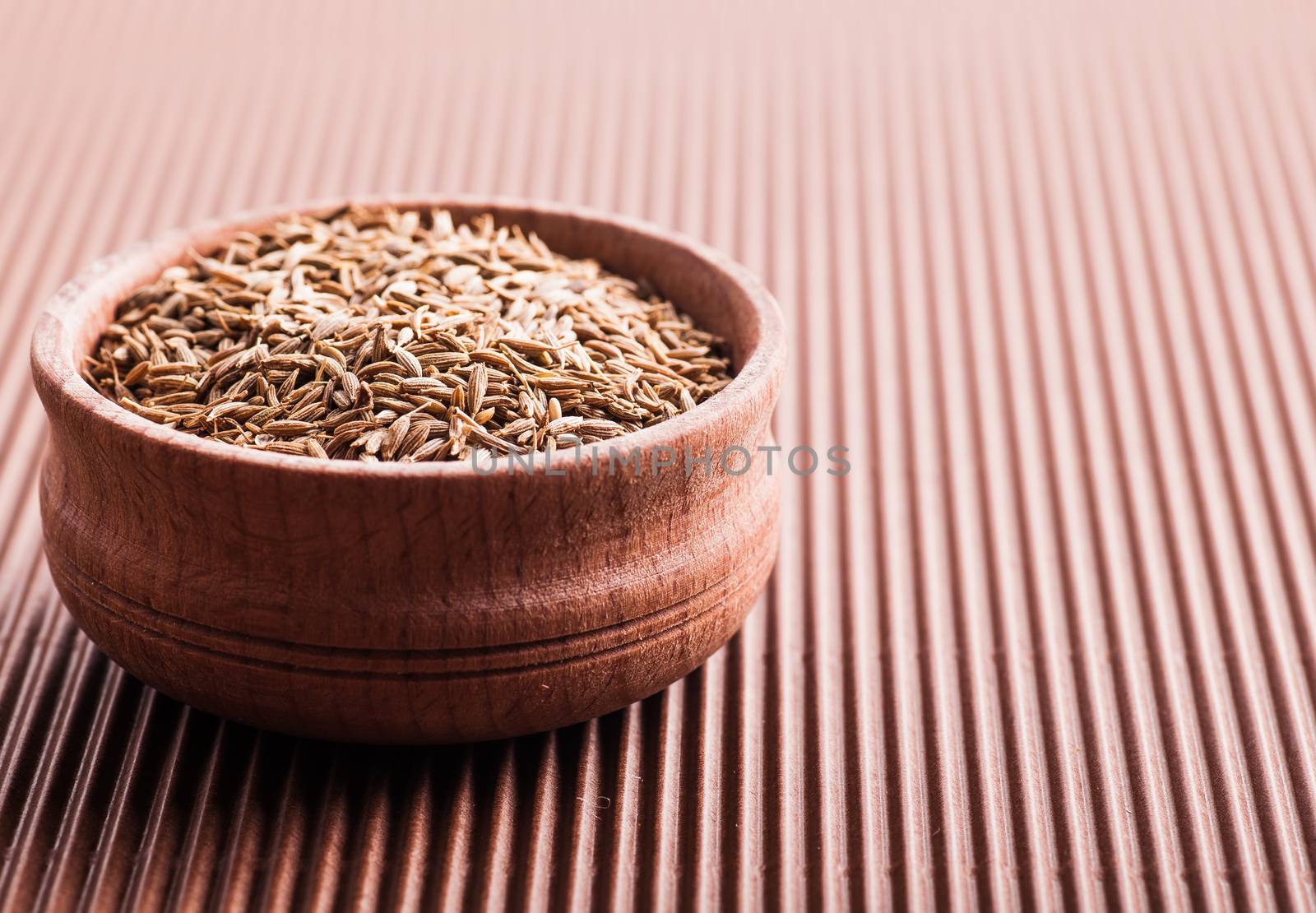 spice cumin in a wooden bowl on a brown background