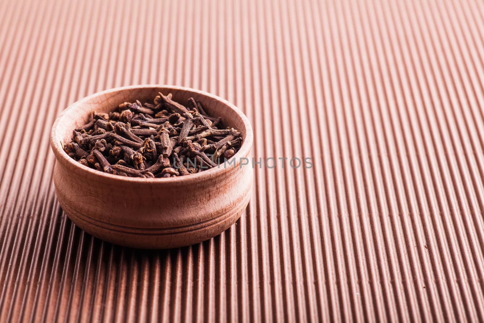 clove in a wooden bowl on a brown background