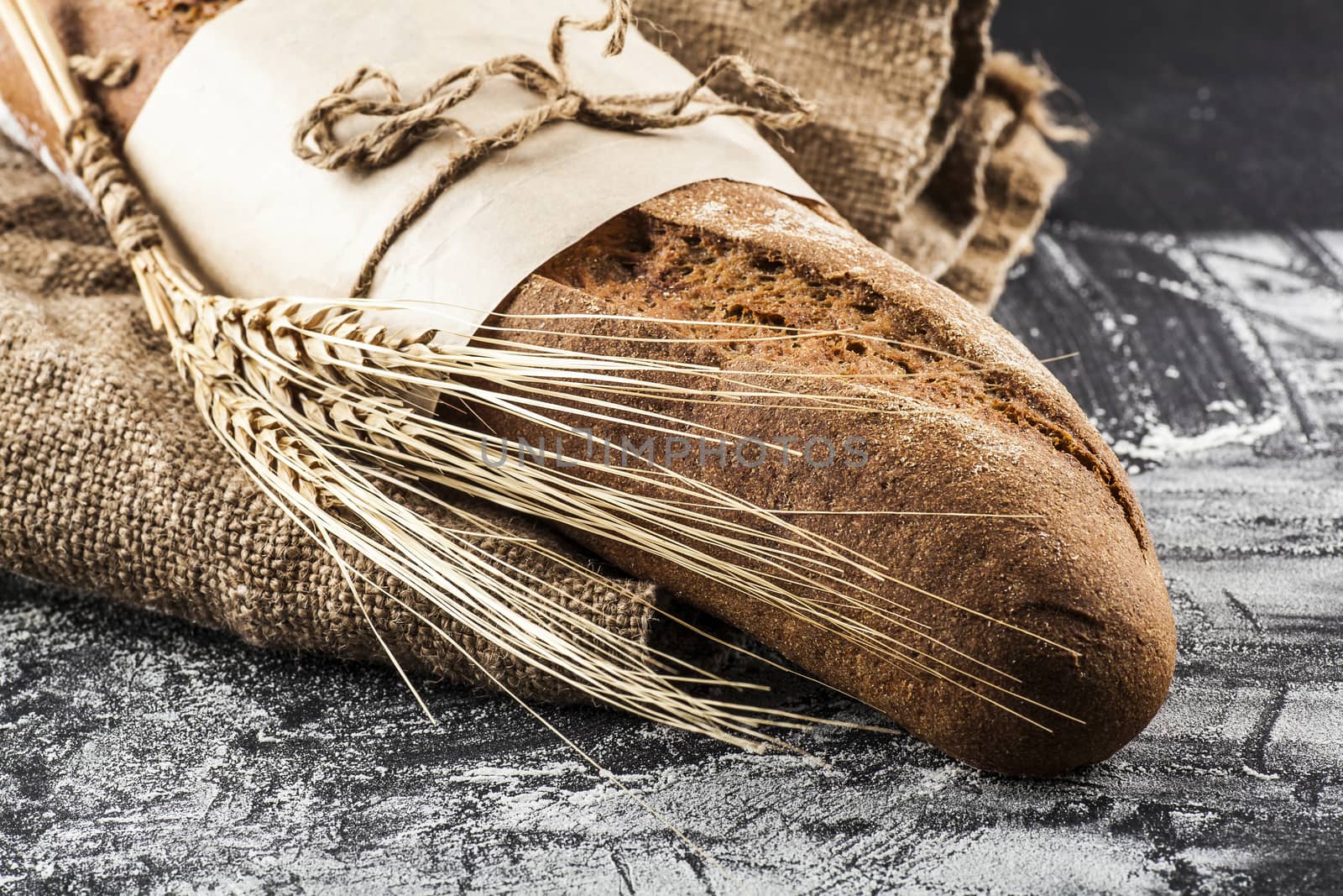 black long loaf with ears of wheat on a dark background with flour