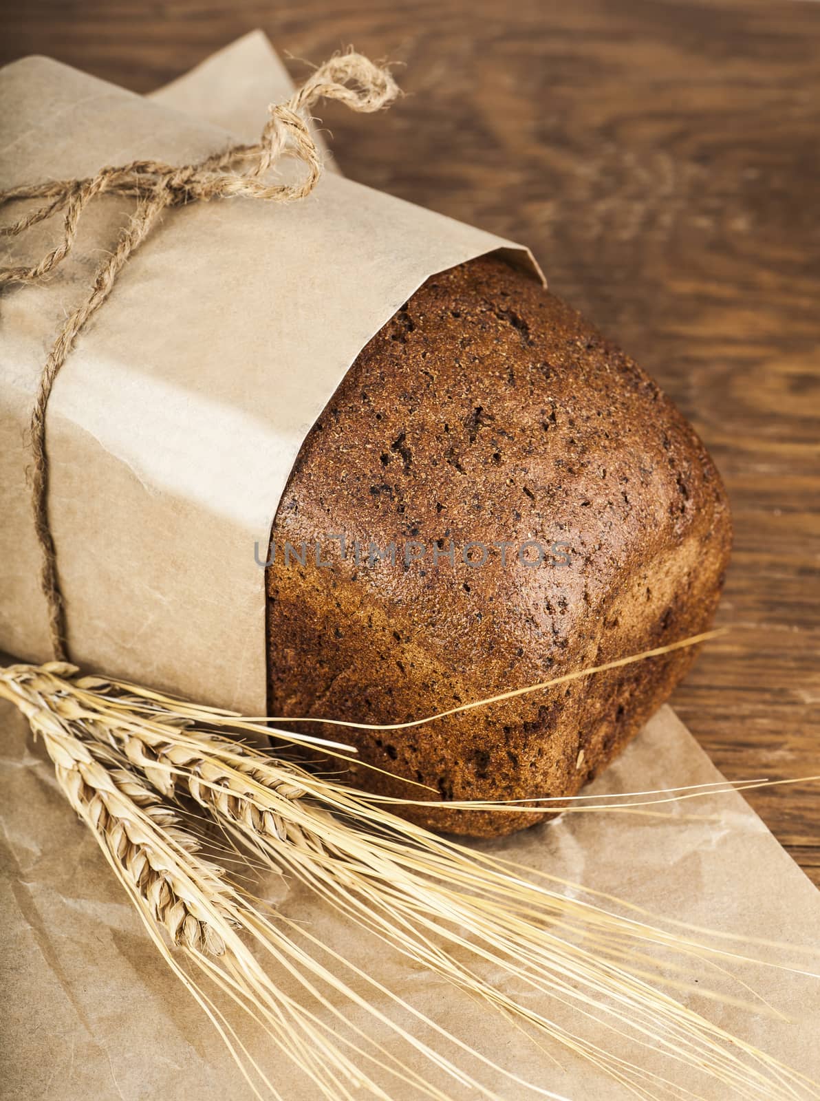 black bread in a paper packing with ears of wheat on the wooden background