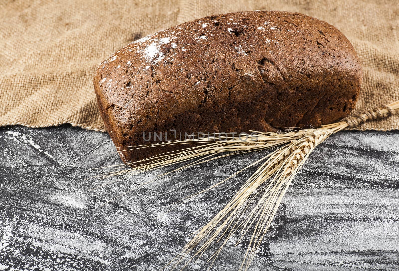 brown bread with ears of wheat on a dark background with flour