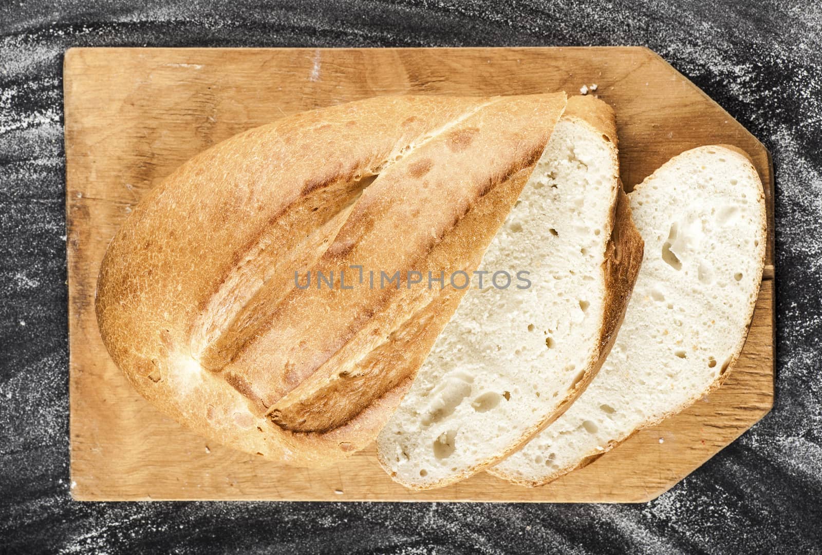 sliced white long loaf on a dark background with flour