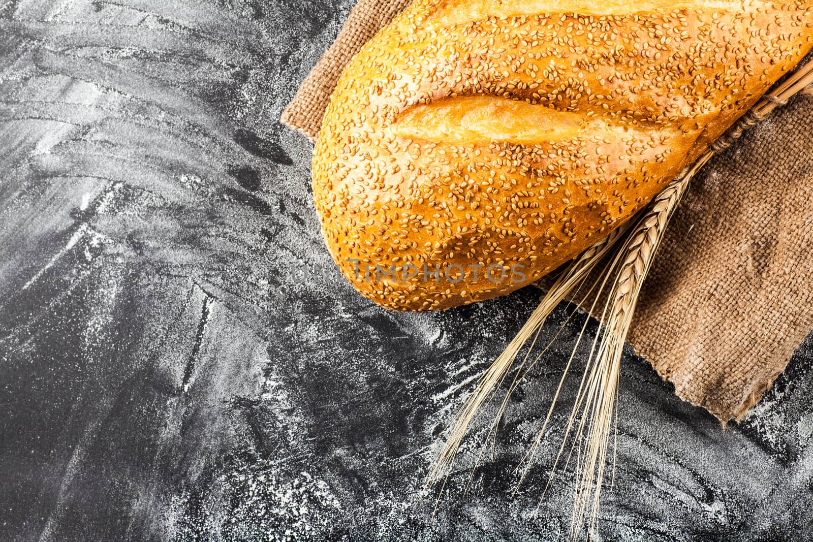 white bread with sesame and wheat ears on dark background