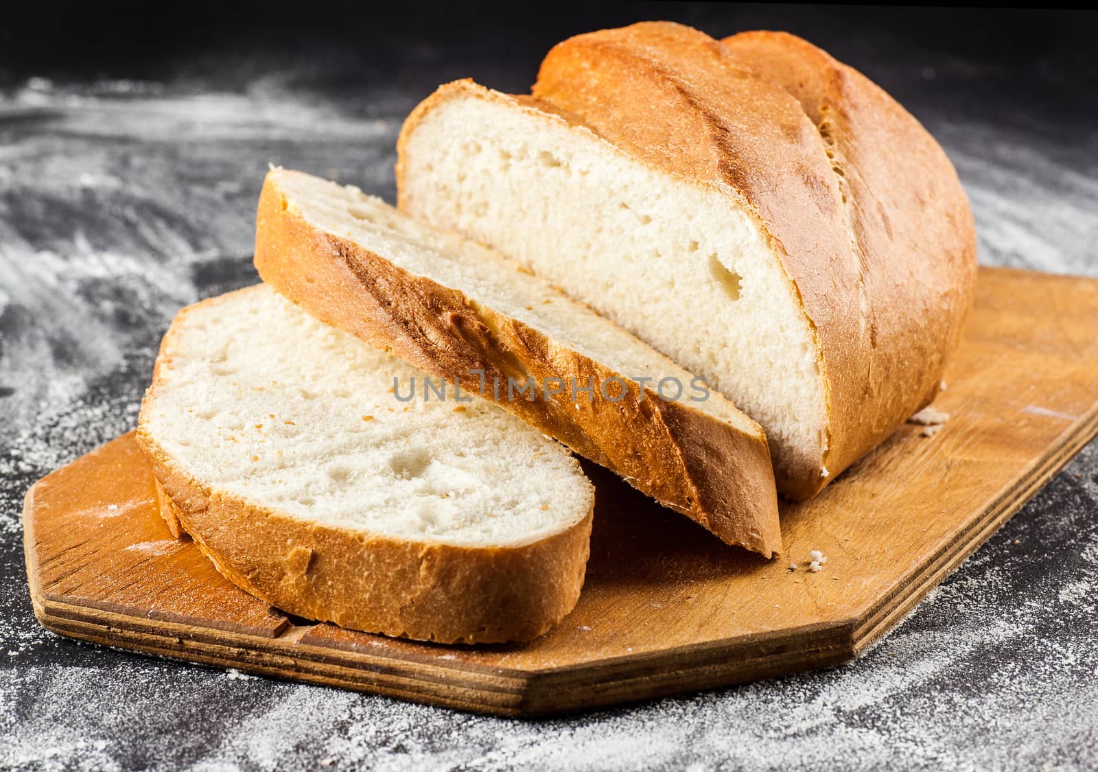 sliced long loaf on a dark background with flour