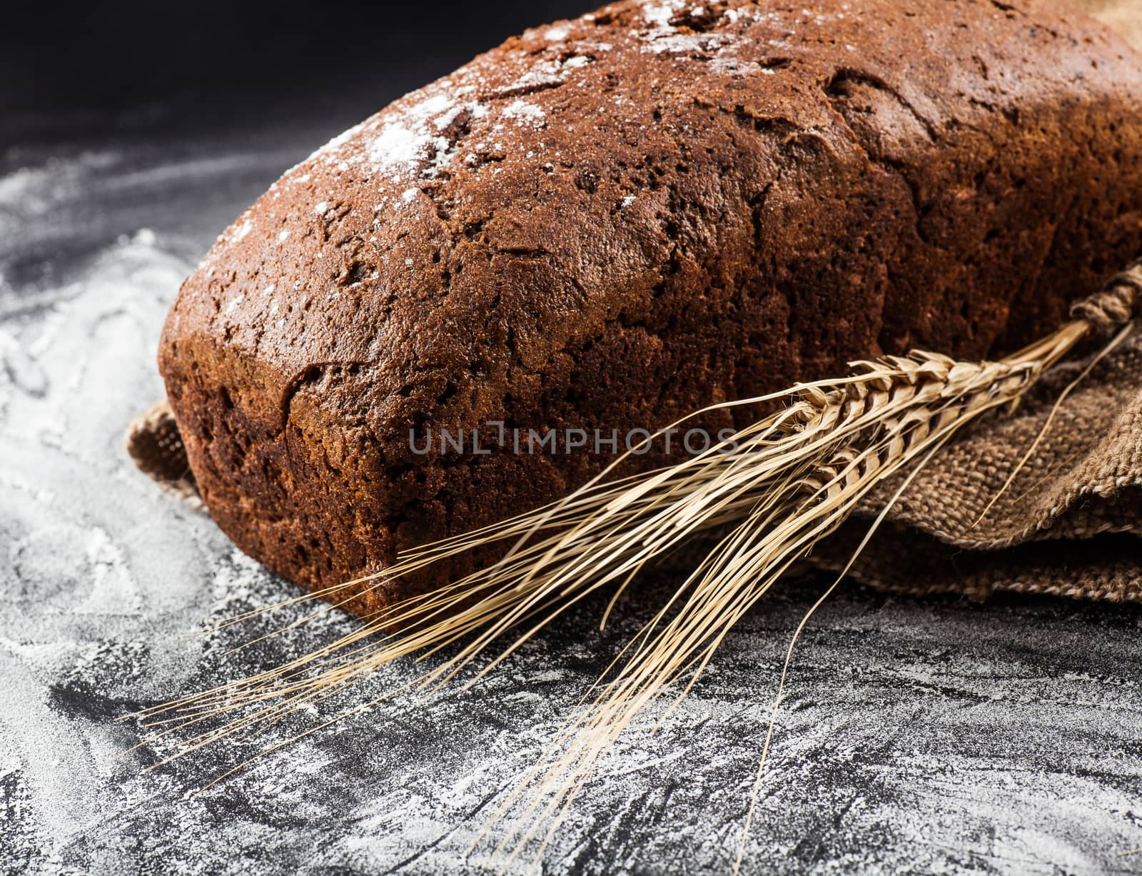 bread with ears of wheat on a dark background with flour