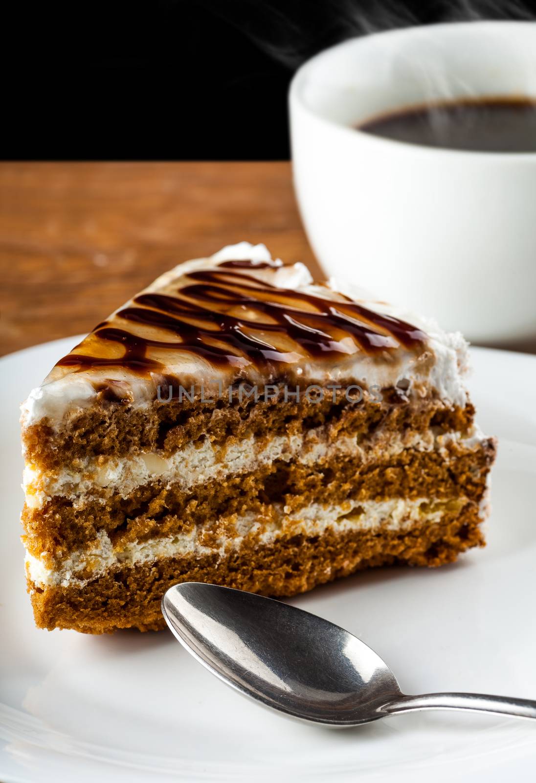 piece of chocolate cake on a plate with a spoon and black coffee on a dark background