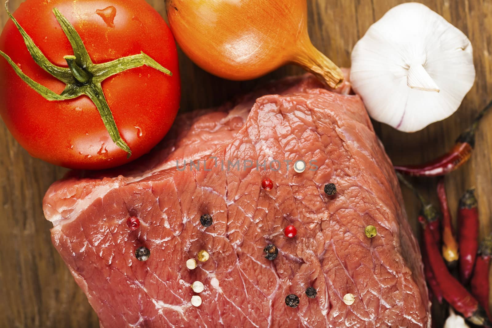 raw fillet of beef with spices and vegetables on wooden background