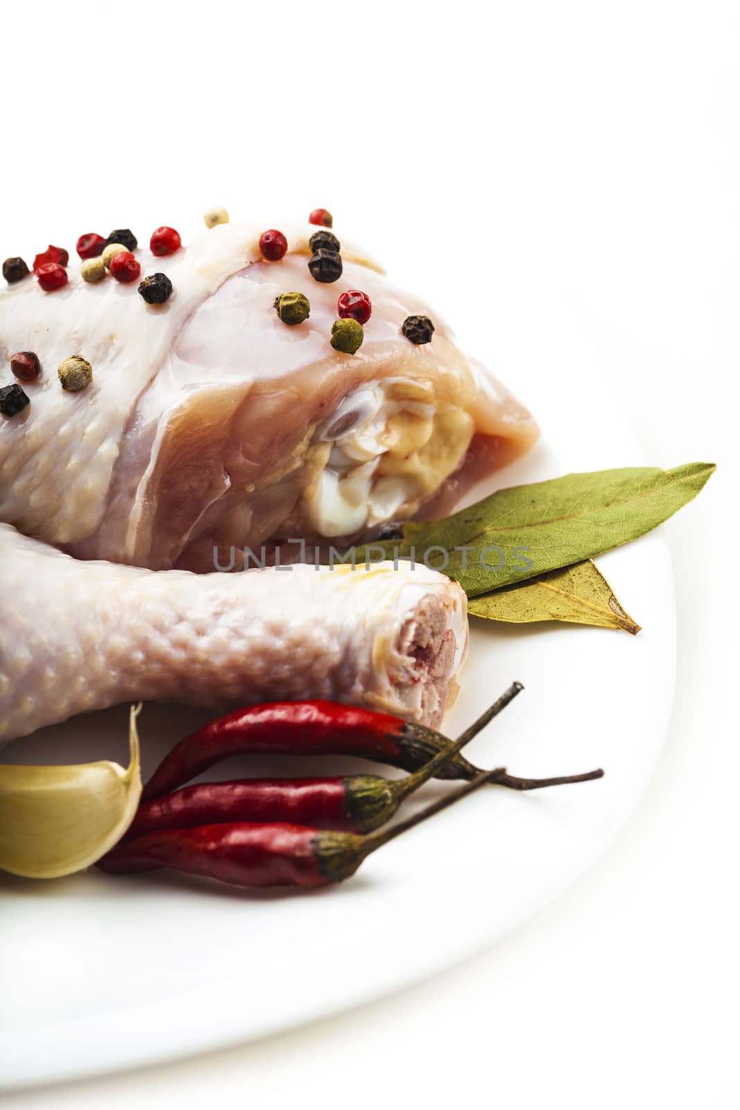 raw chicken legs on the plate with spices, white background