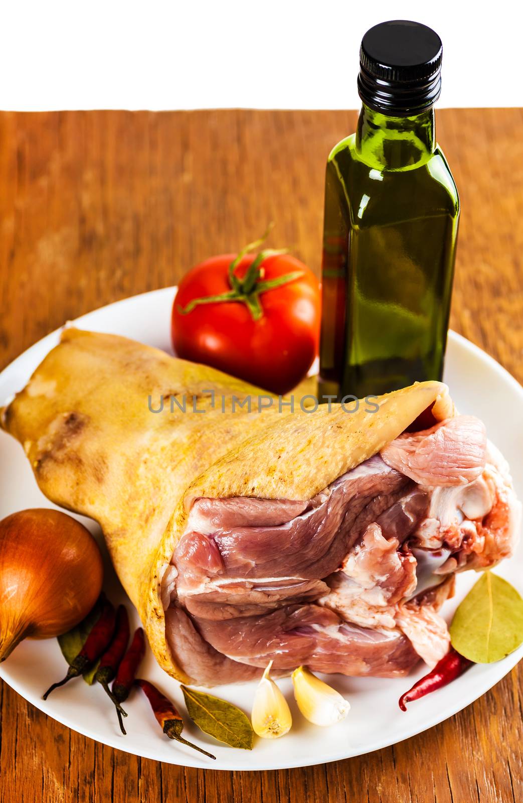 raw pork shank on a plate with spices and vegetables, a wooden background