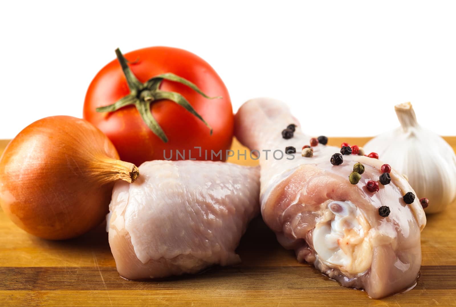 marinated chicken legs on a wooden board with spices and vegetables, white background