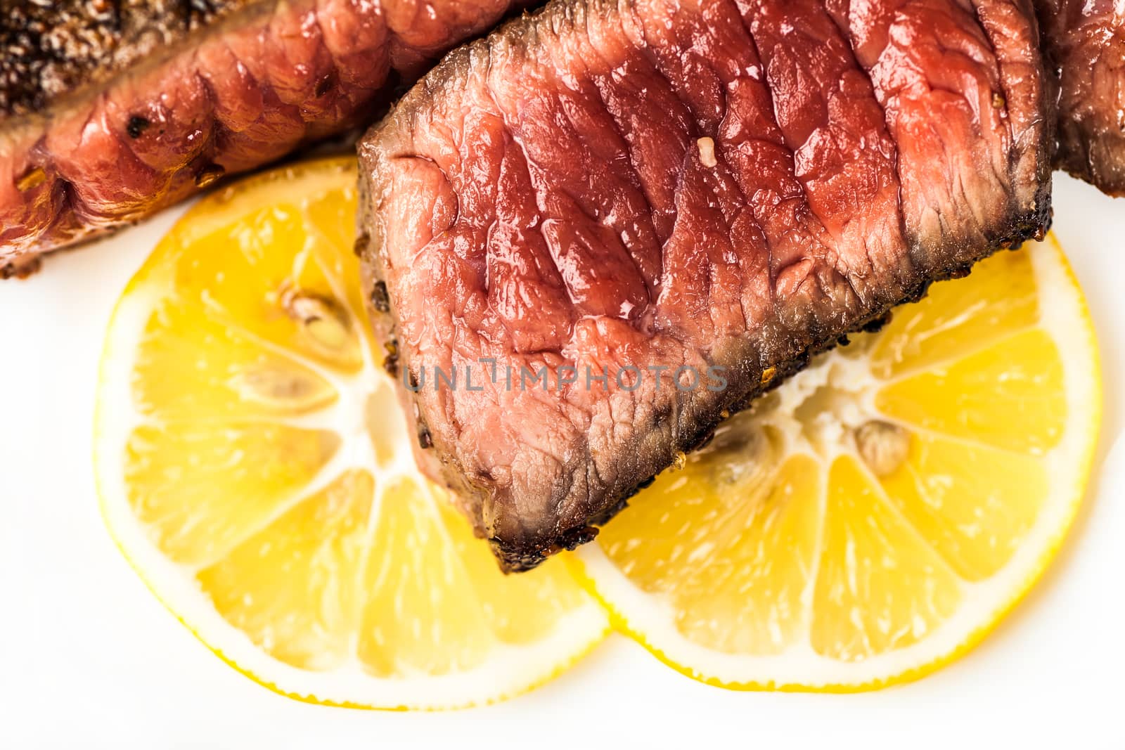 Sliced roasted meat with slices of lemon on a white plate