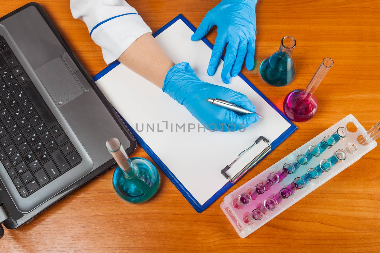 assistant of writes beside the laptop and test tubes with reagents 