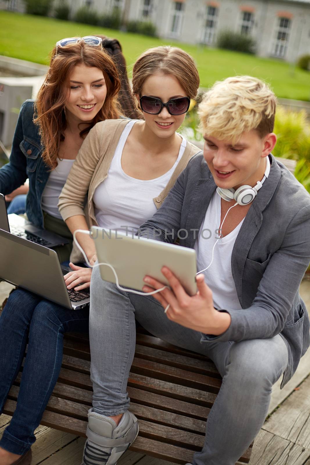 summer, education, technology and people concept - group of students or teenagers with laptop computers sitting on bench outdoors