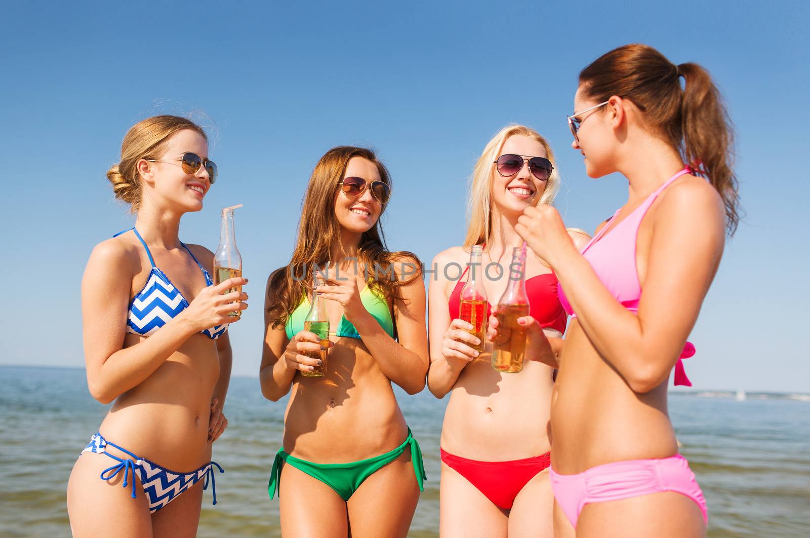 summer vacation, holidays, travel and people concept - group of smiling young women sunbathing and drinking on beach