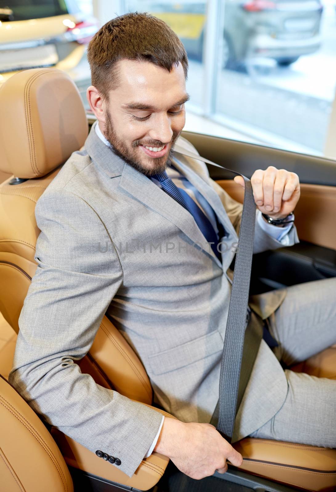 happy man sitting in car at auto show or salon by dolgachov