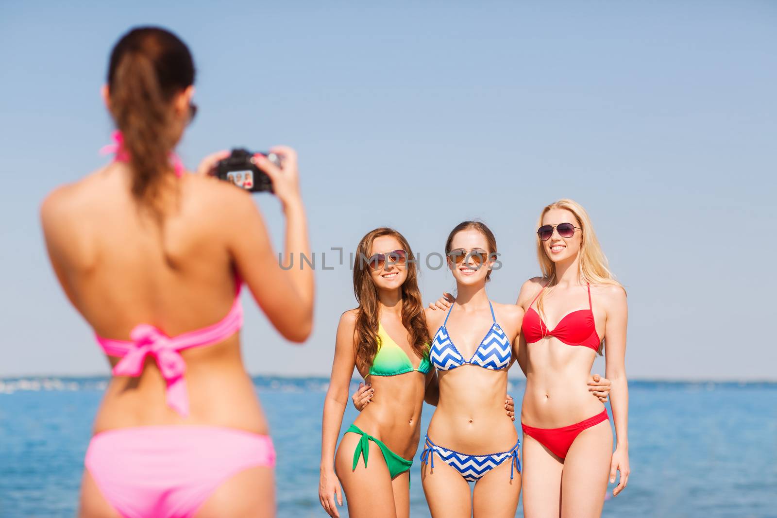 group of smiling women photographing on beach by dolgachov