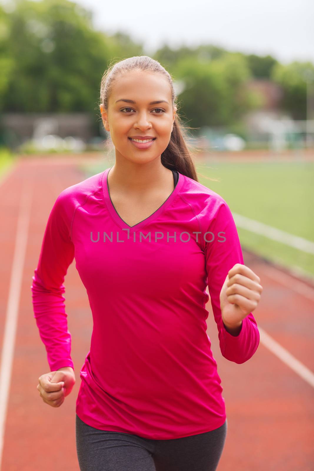 smiling woman running on track outdoors by dolgachov