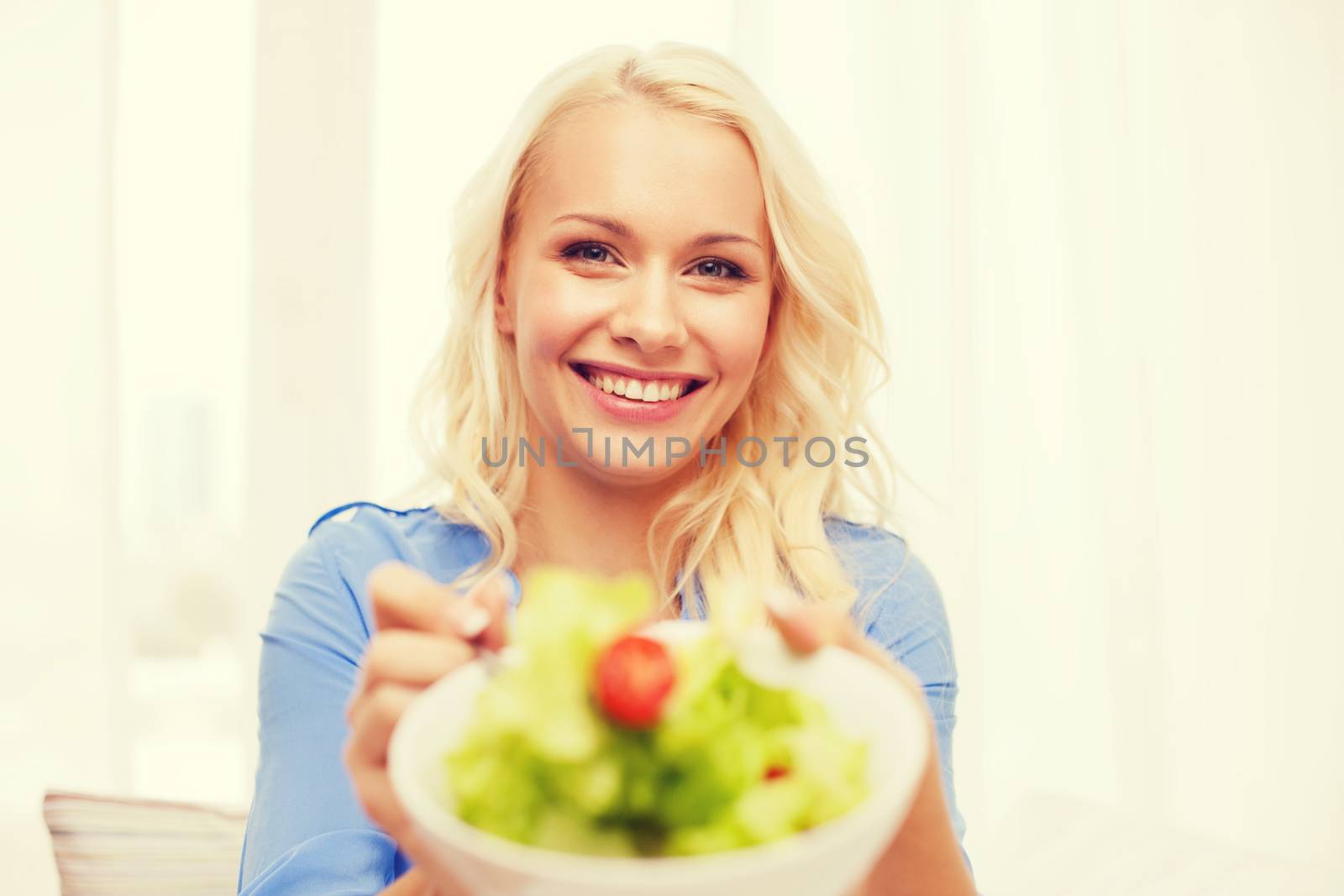 smiling young woman with green salad at home by dolgachov