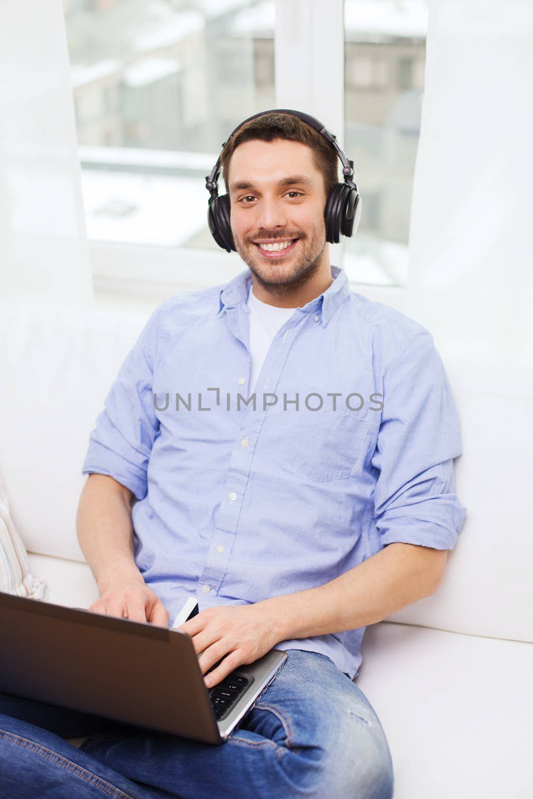 technology, home, music and lifestyle concept - smiling man with laptop and headphones at home