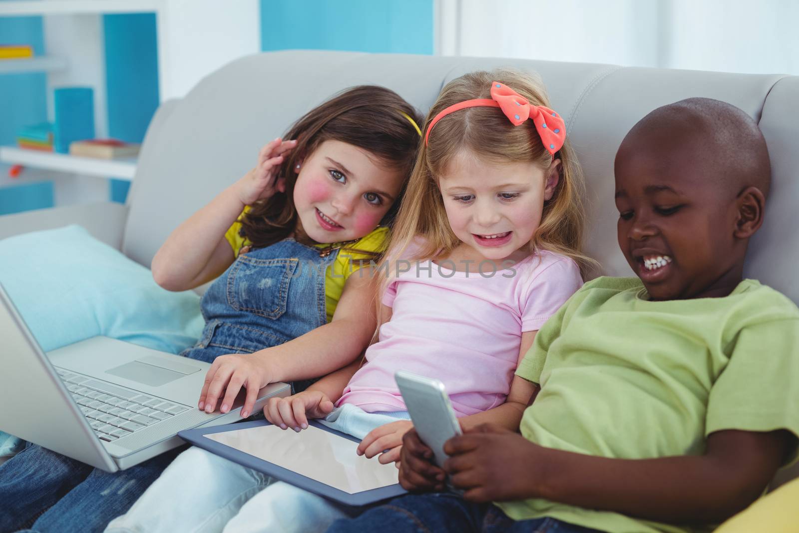 Happy kids sitting together with a tablet and laptop and phone by Wavebreakmedia