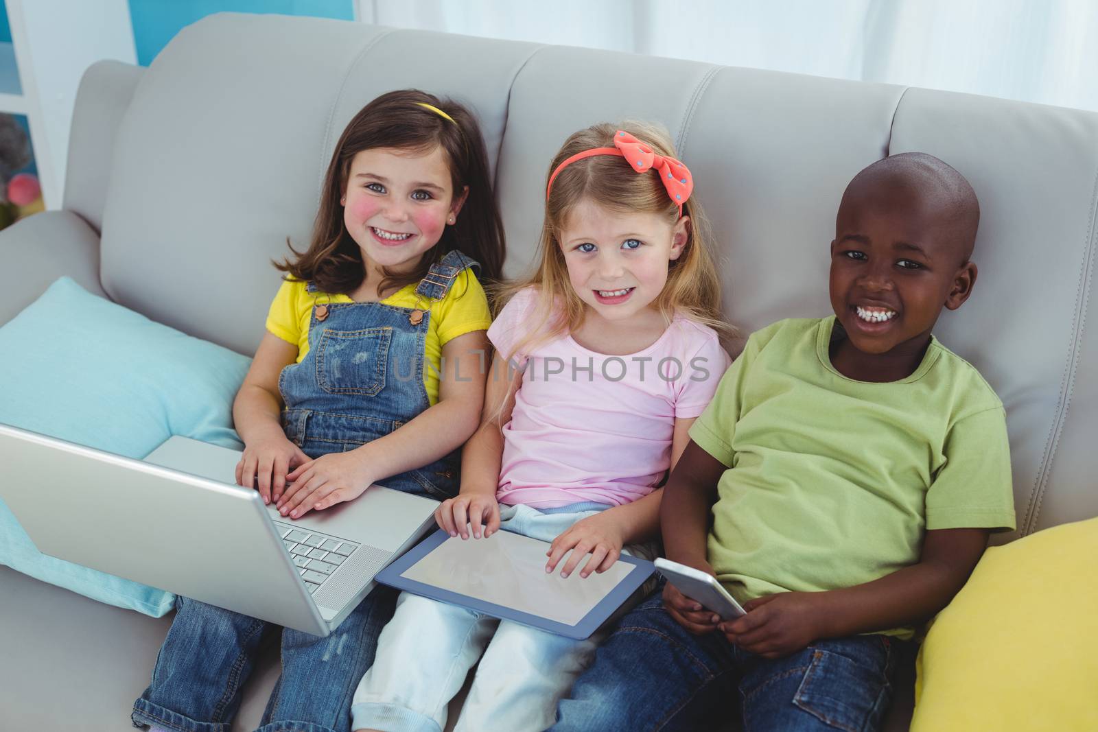 Happy kids sitting together with a tablet and laptop and phone on the couch