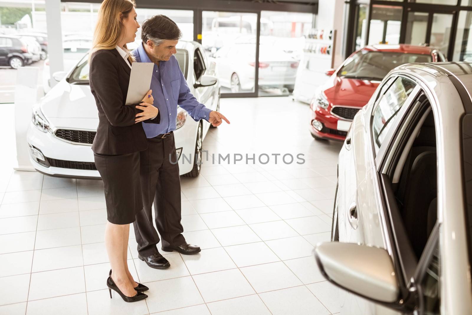 A man showing a car to the saleswoman at new car showroom