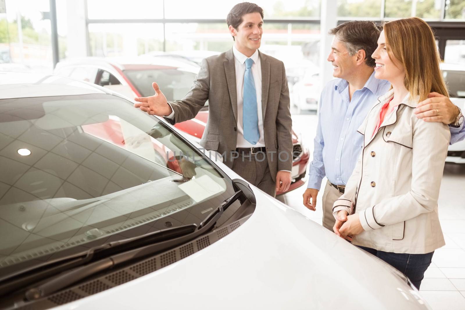 Smiling businessman presenting a car at new car showroom