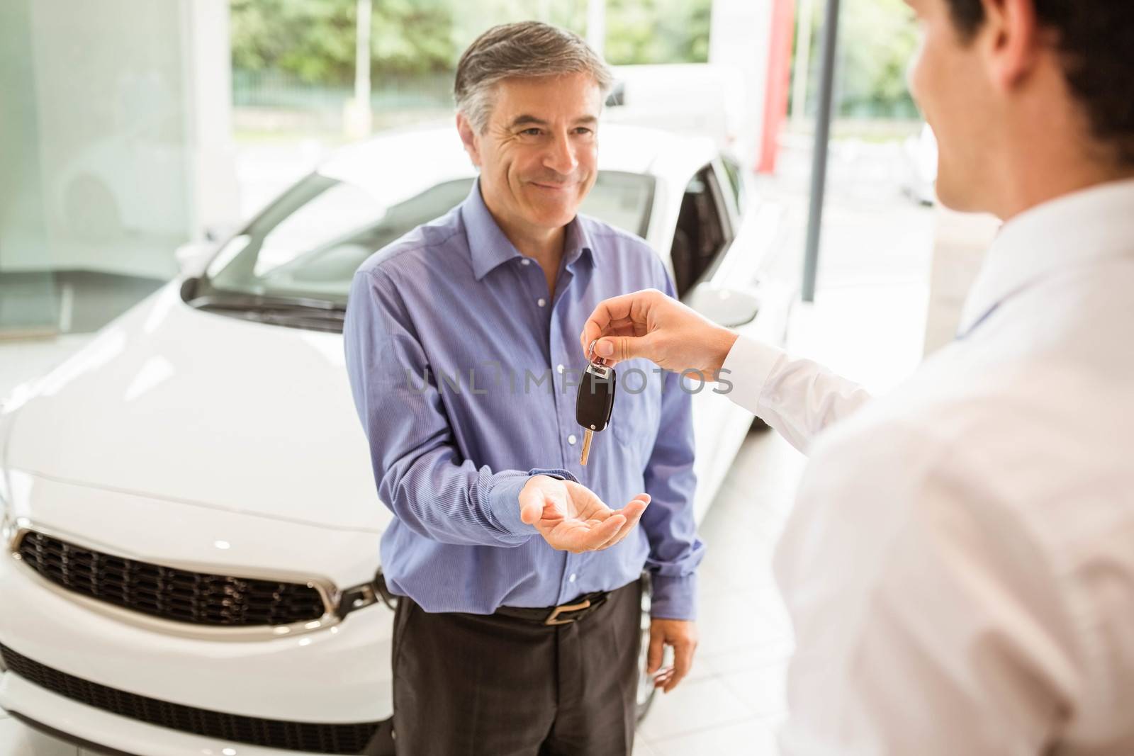 Businessman giving car key to a customer at new car showroom