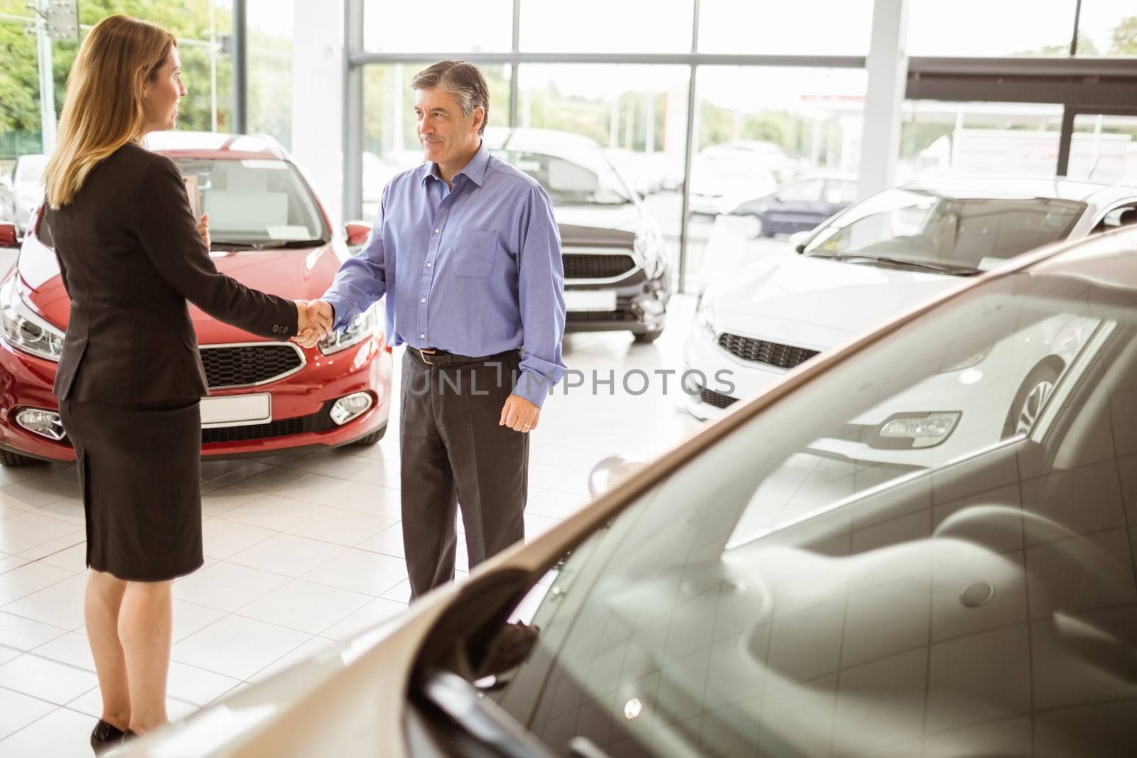 Person shaking hands in front of a car at new car showroom