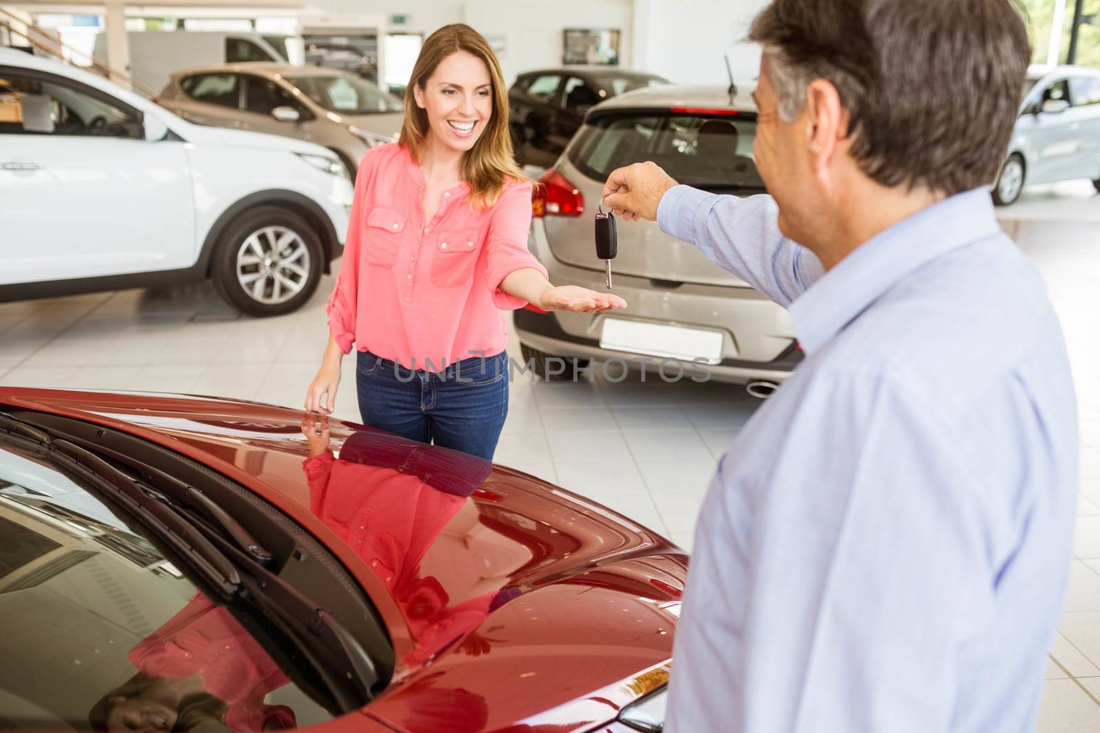 Smiling businessman giving car key to happy customer at new car showroom