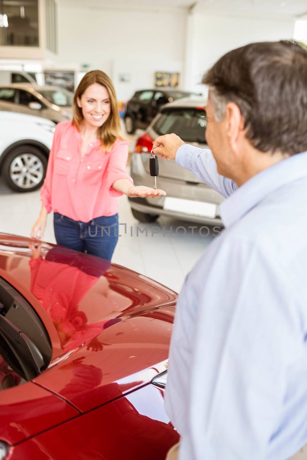 Smiling businessman giving car key to happy customer at new car showroom