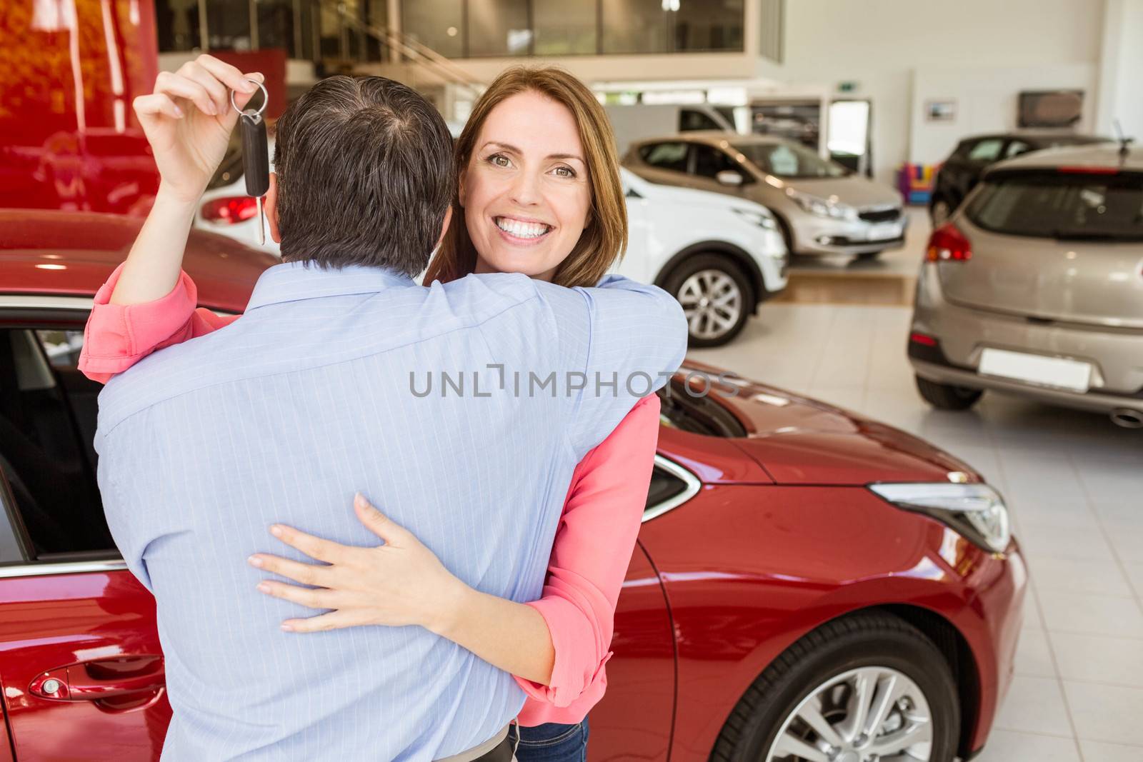 Smiling woman holding key while hugging her husband at new car showroom