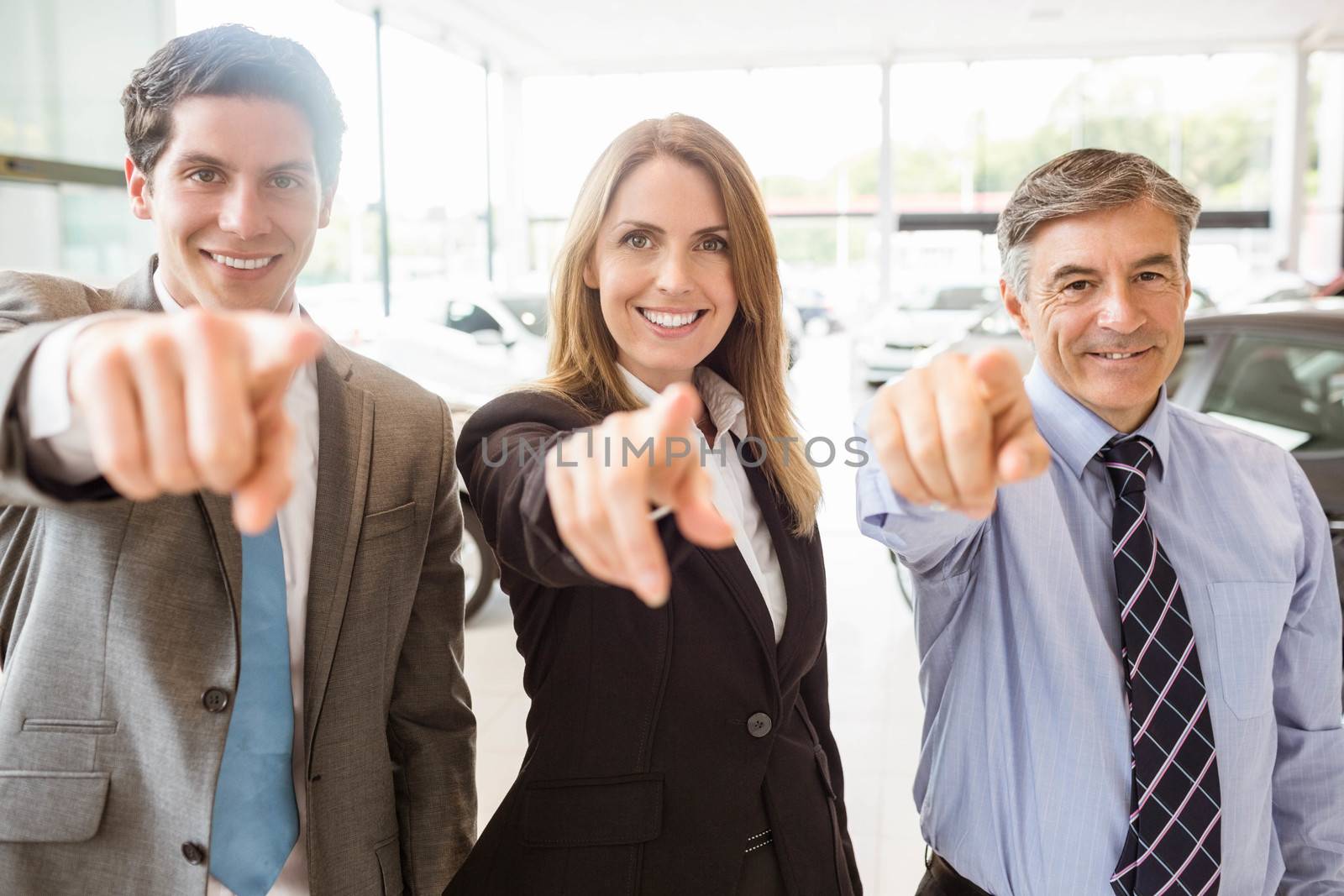 Group of smiling business team pointing together at new car showroom