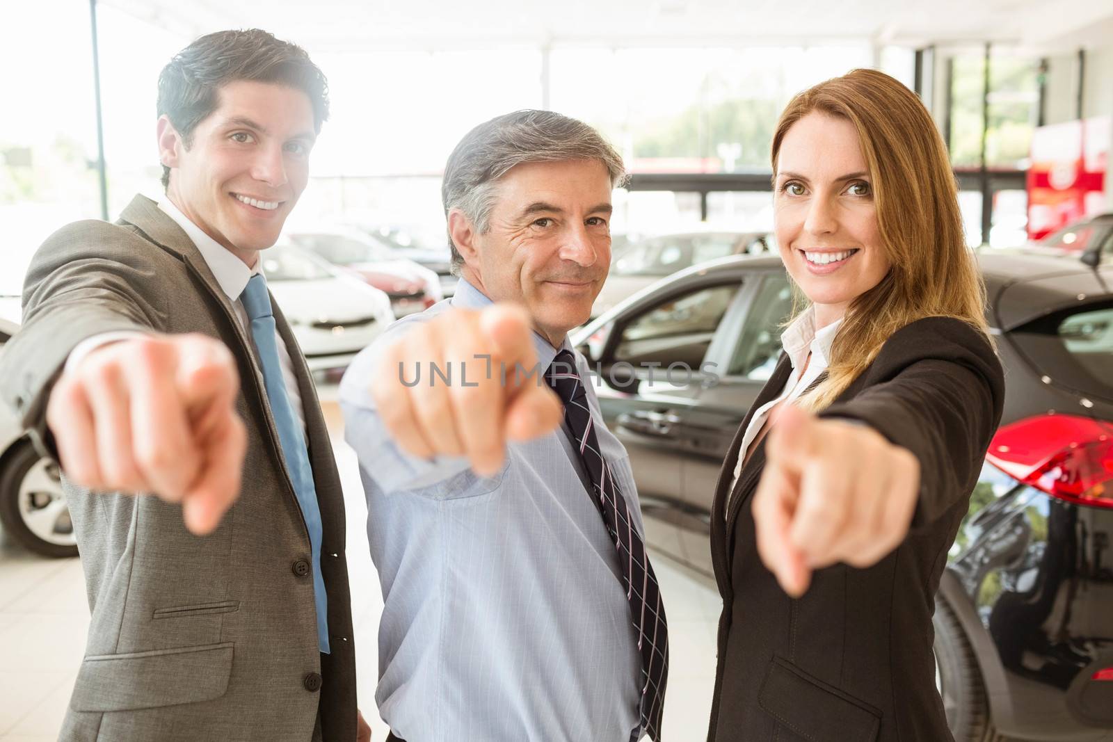 Group of smiling business team pointing together at new car showroom