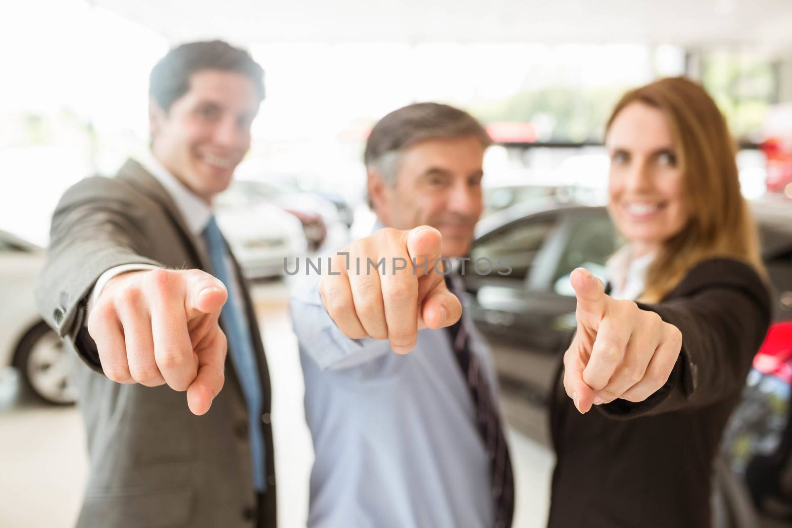 Group of smiling business team pointing together at new car showroom