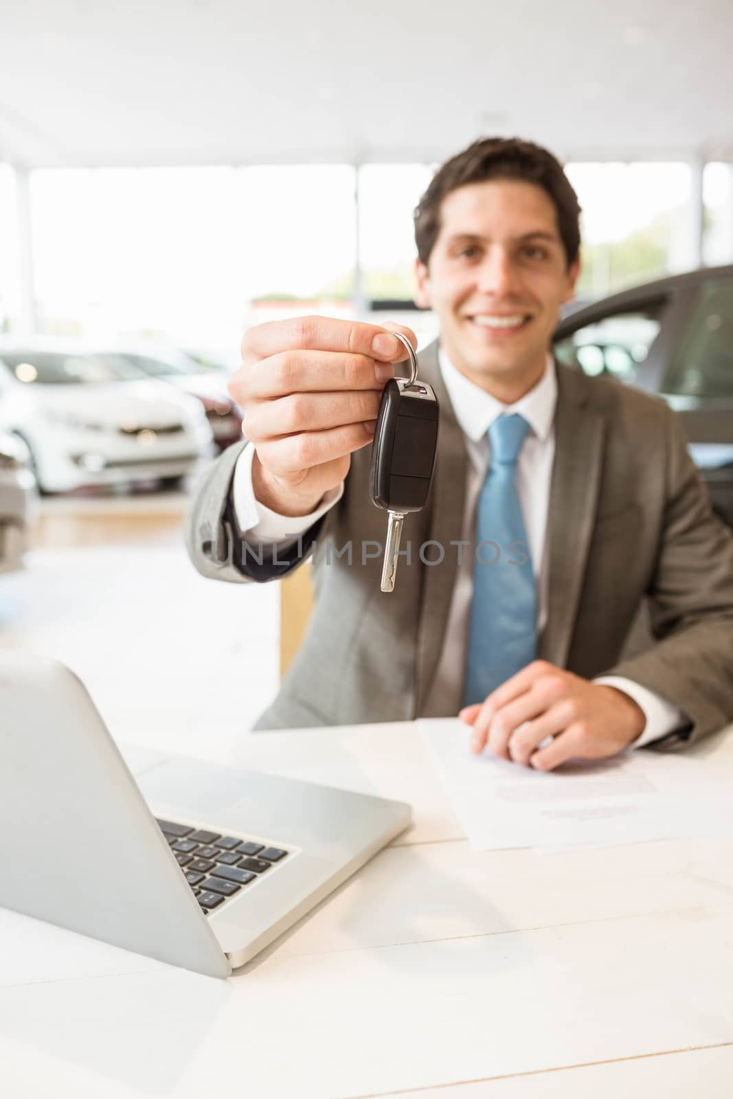 Smiling salesman holding a customer car key at new car showroom