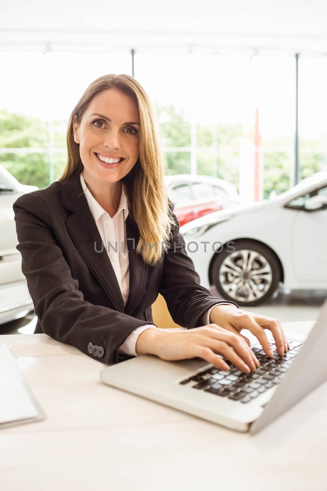 Smiling saleswoman typing on her laptop at new car showroom